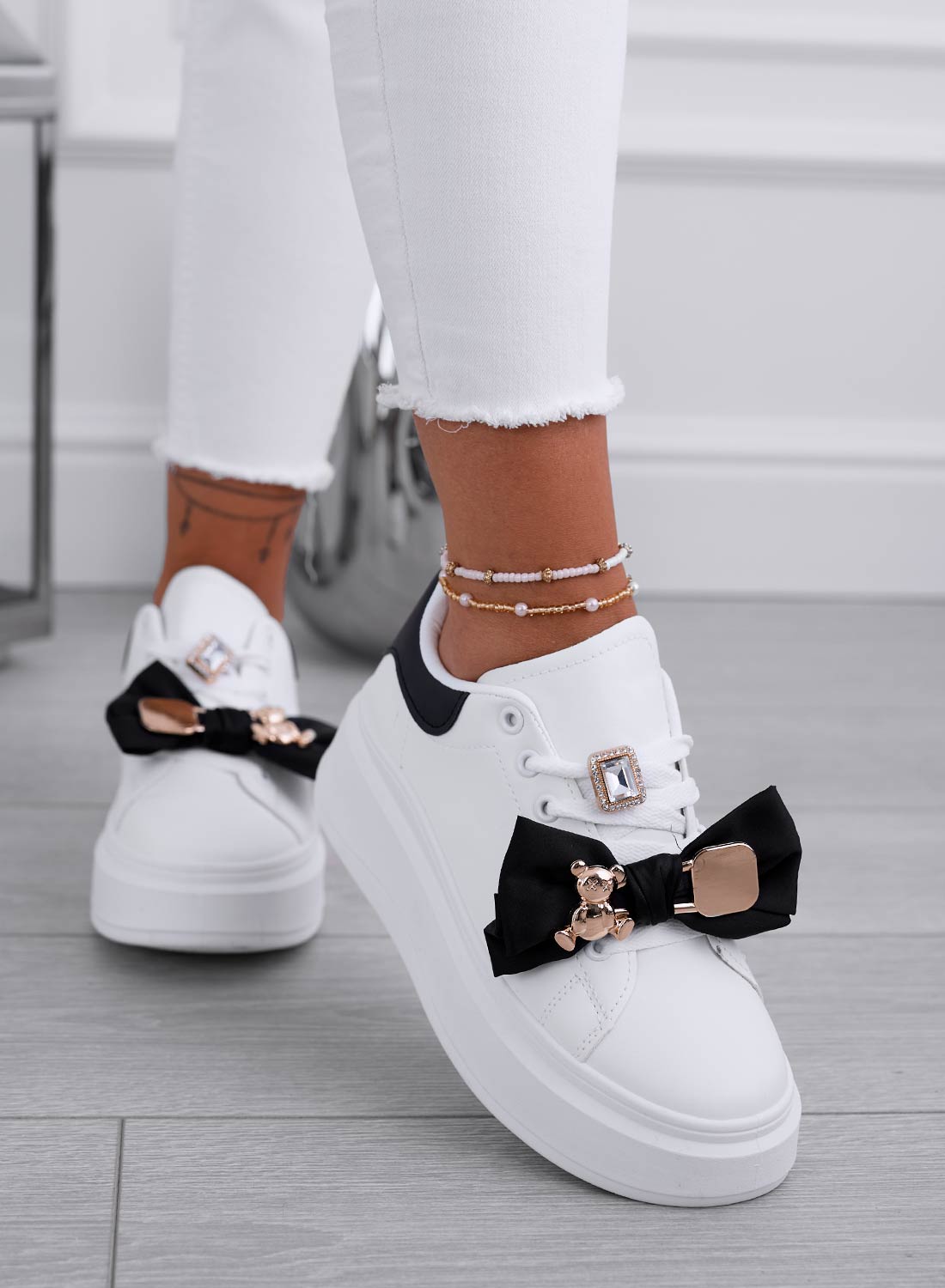 White sneakers with black bow and gold teddy brooch